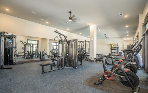 A gym with a variety of equipment including treadmills, weights, and a bench at The Ashton at East Park Apartments, Kennesaw, Georgia